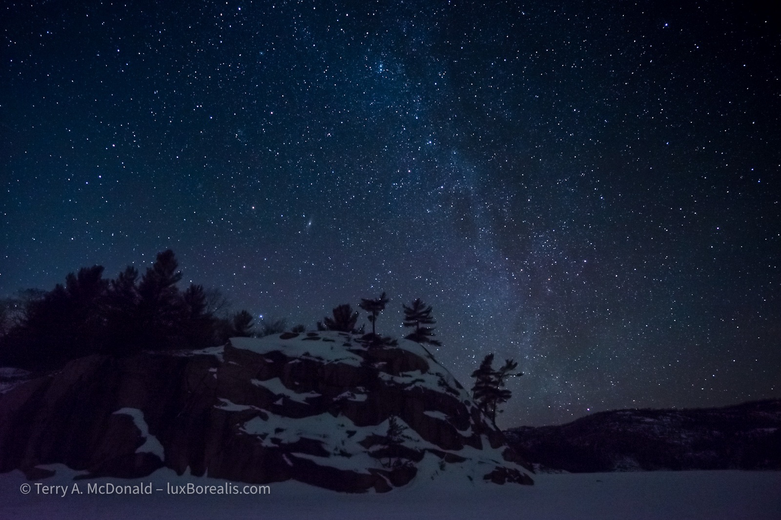 Night Sky, Winter, George Lake, Killarney
The Milky Way makes an appearance in the millions of stars, white dots on a slate of dark blue, with the George Lake granite monolith in the foreground. ©Terry A. McDOnald – luxBorealis.com