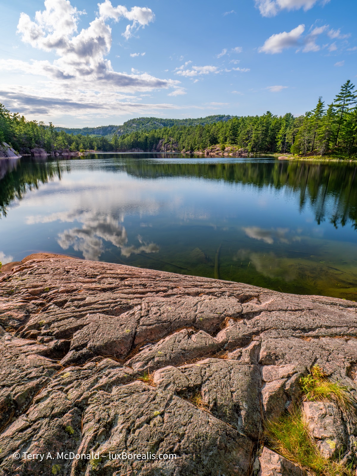 A view across A.Y. Jackson Lake with  eroded pink granite int he foreground under a blue sky with a few clouds.