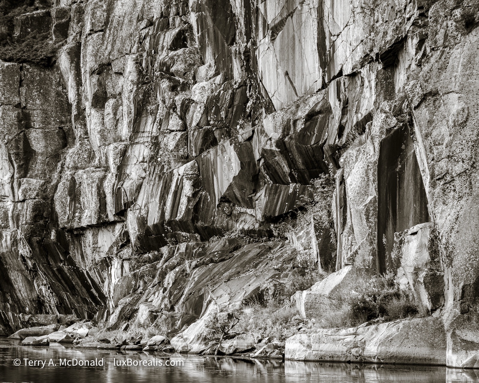 A black-and-white photograph showing the eroded cliffs of pink Killarney granite along the shore of lake Sheguiandah.